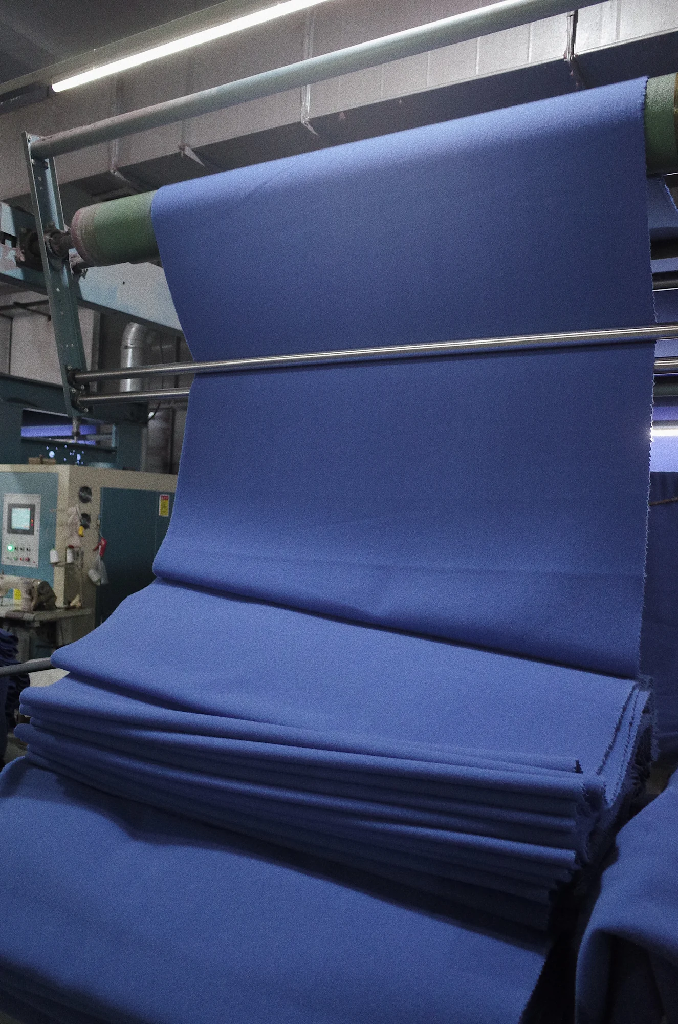 Blue finished fabric moving through finishing equipment at Fred Textile