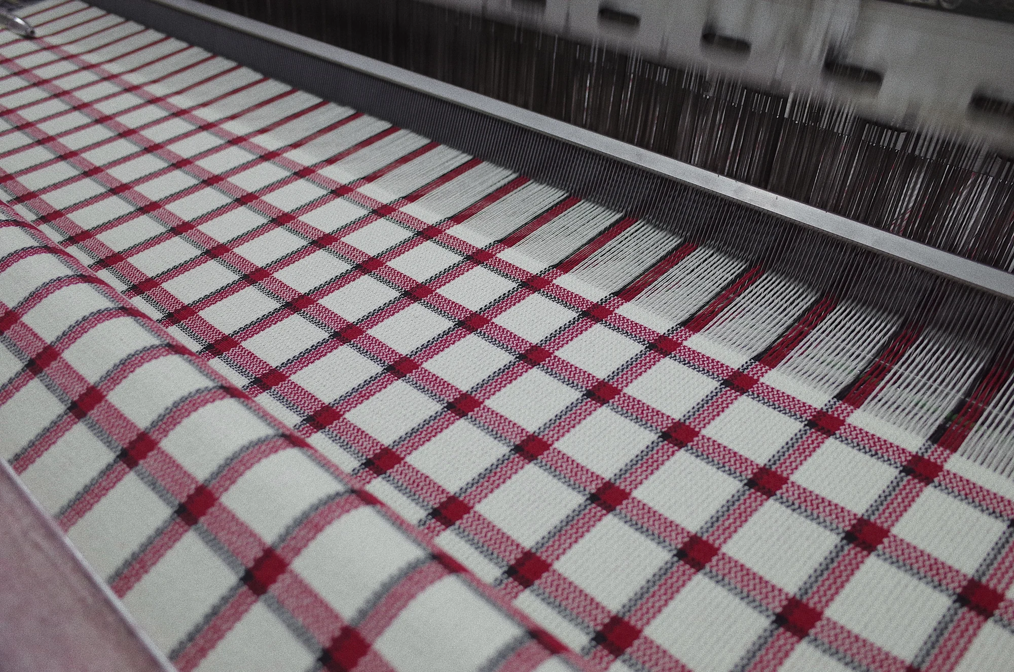 Red and black tartan fabric being woven on a loom at Fred Textile